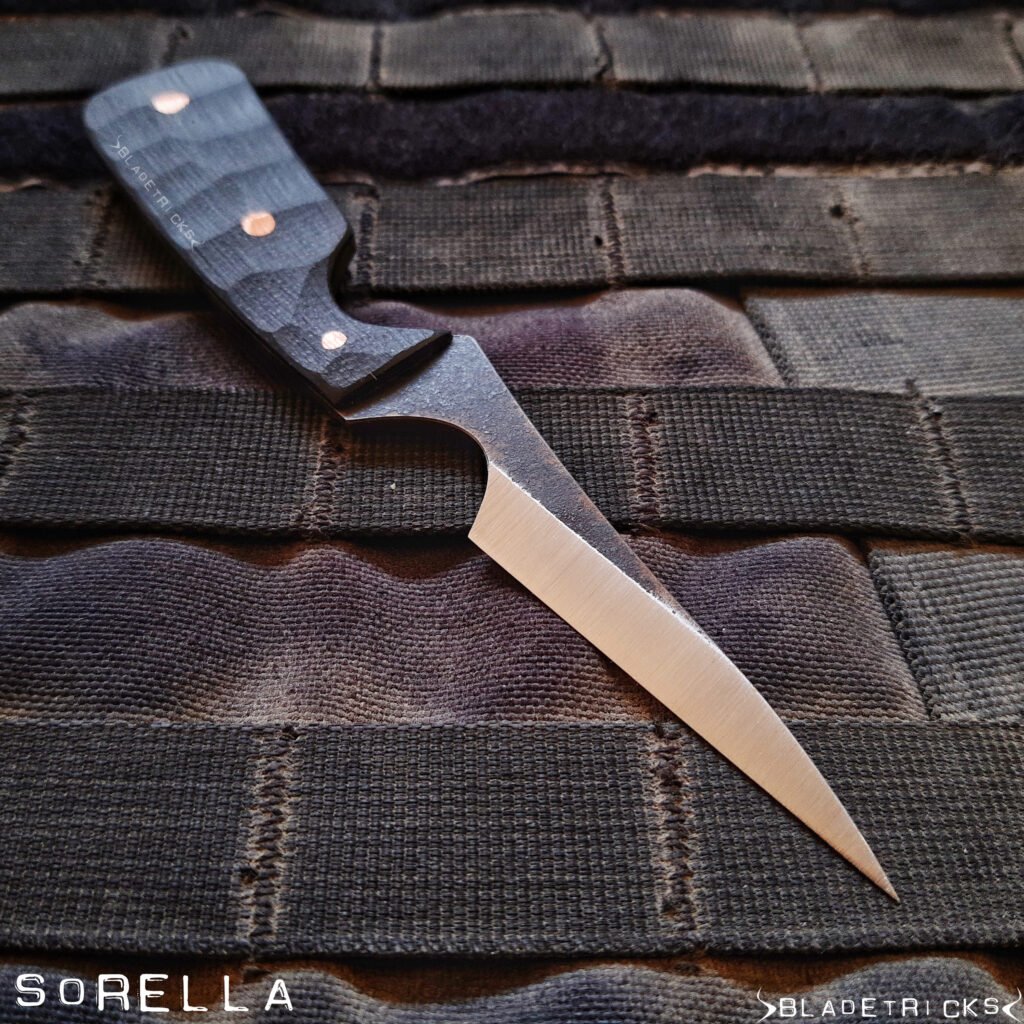 Bladetricks Sorella pikal knife with a pinky choil at the base of the blade, dark fluted handle scales with copper pins, resting on black webbing.