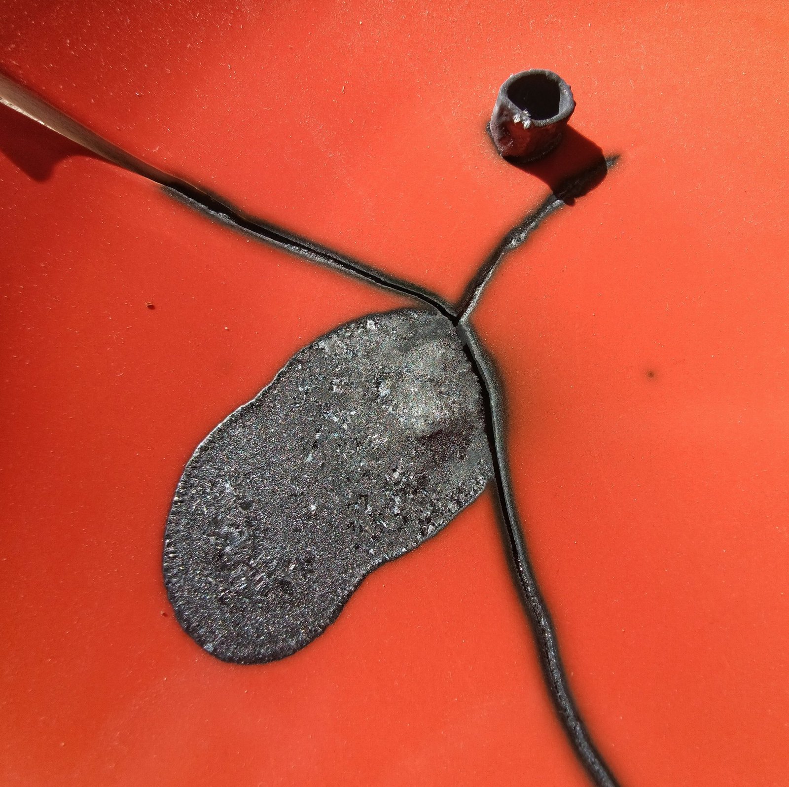 Melted copper puddle solidified next to a partially melted copper pipe ring on a red refractory dish, from a kiln calibration test